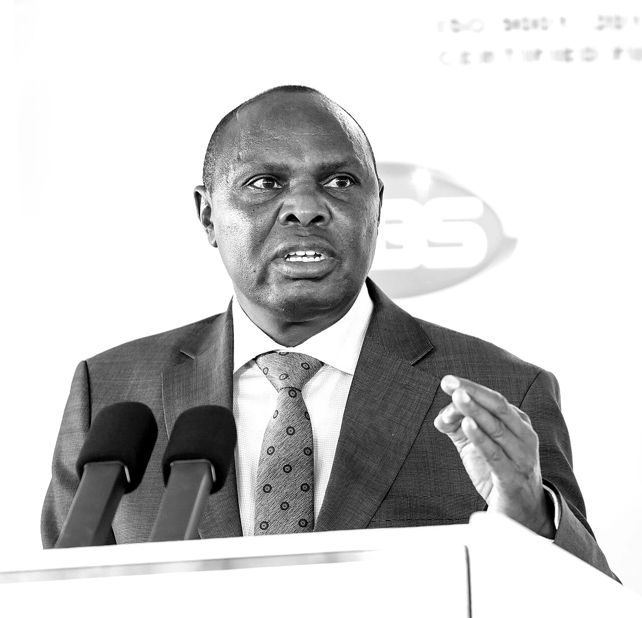 Felix Koskei speaking at a podium in a formal black-and-white portrait