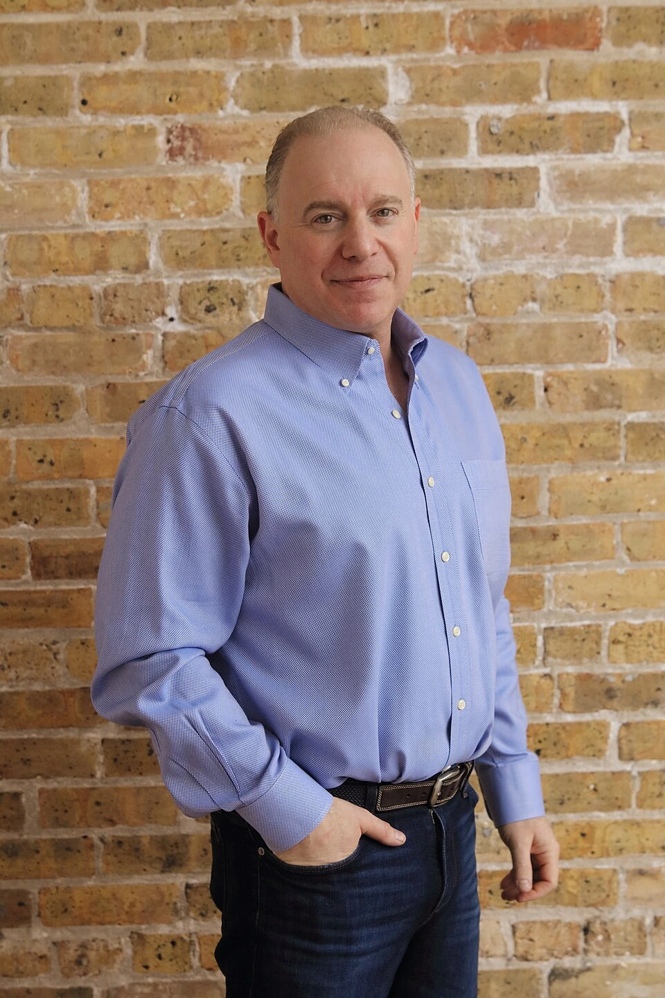 Portrait of Cary Kochman standing in front of a brick wall wearing a blue shirt
