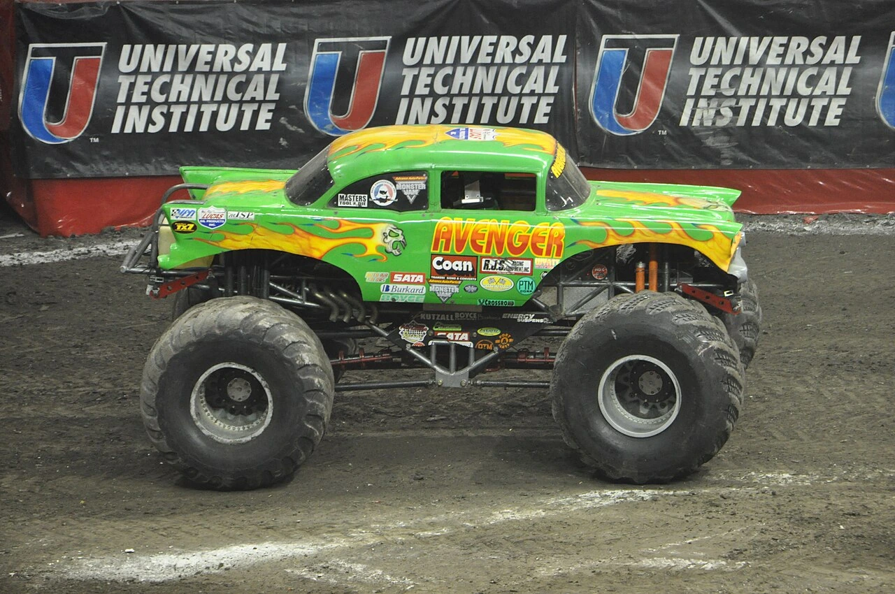 Monster truck Avenger on a dirt arena floor, side view with green and yellow body and sponsor banners behind it